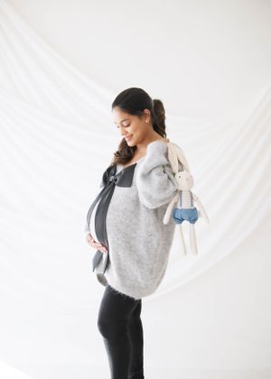 Side view maternity photo showing grey sweater and black bow detail against white backdrop.