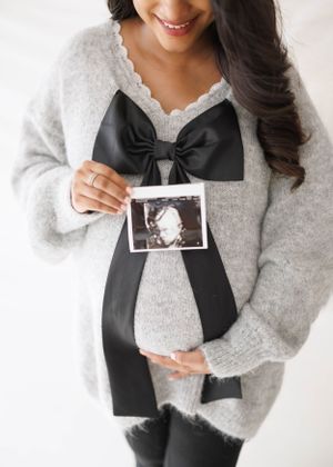 Close-up shot showing grey sweater with black bow and ultrasound photo.