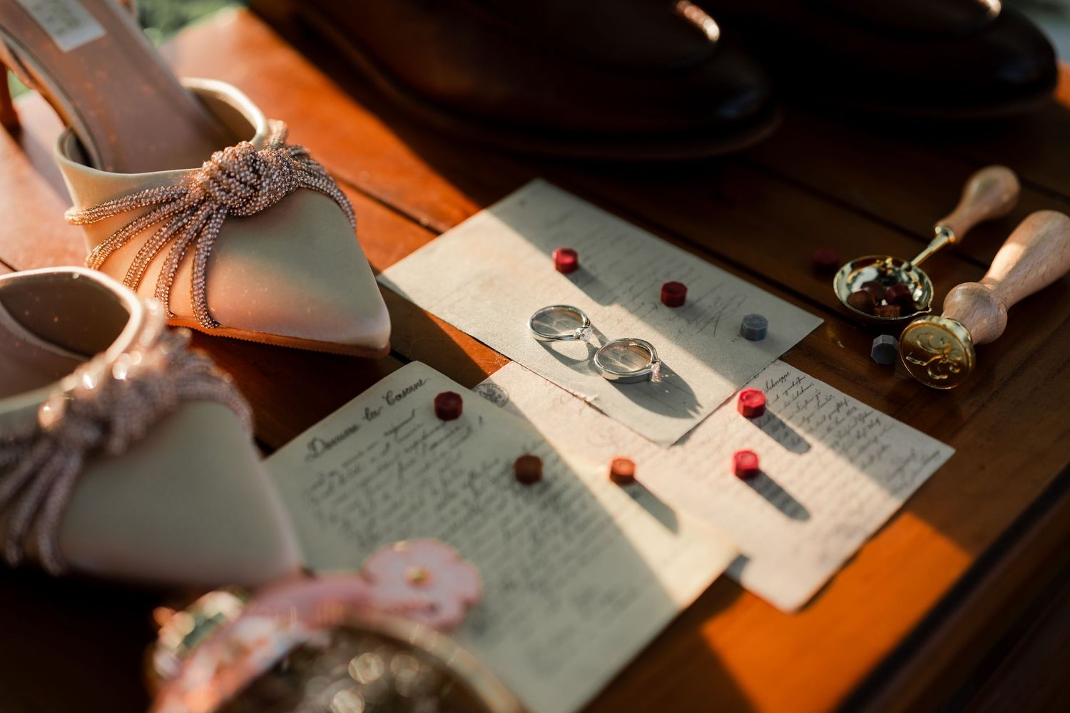Wedding details including bridal shoes and invitation cards arranged on a wooden surface.