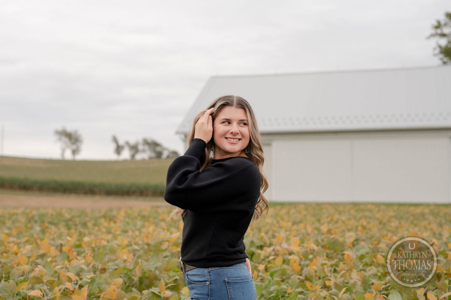 Portrait session in a rural field with white barn and fall foliage.
