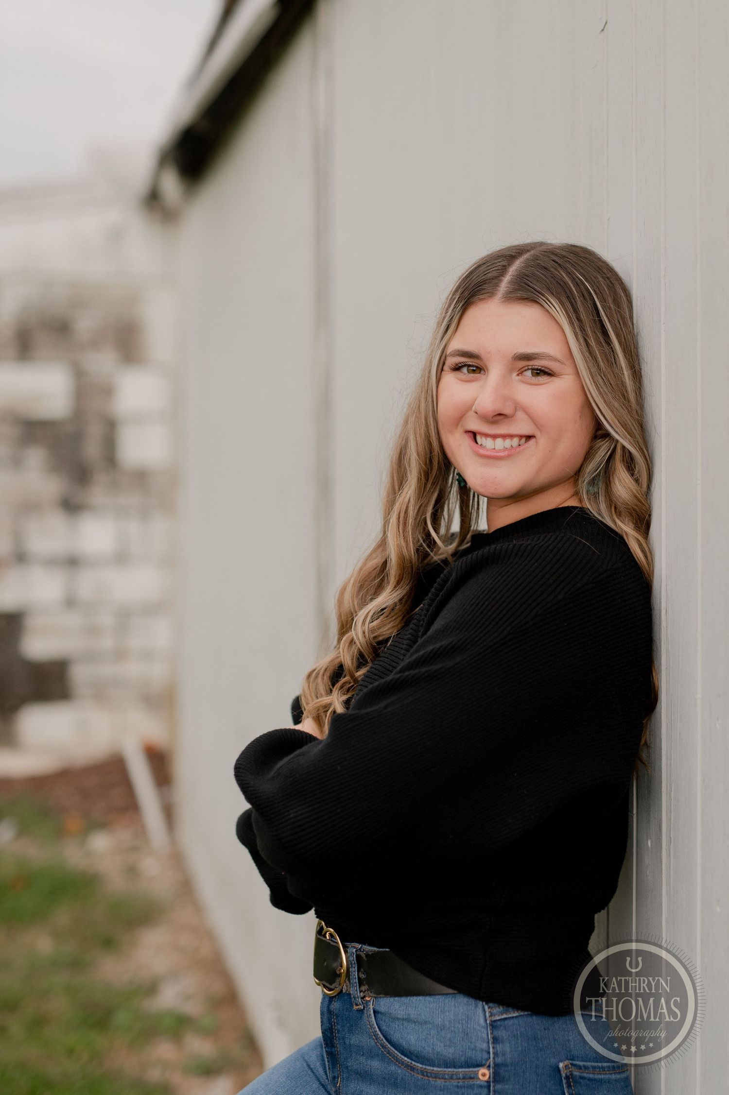 Casual portrait against white wall showing warm smile and relaxed pose in black sweater.