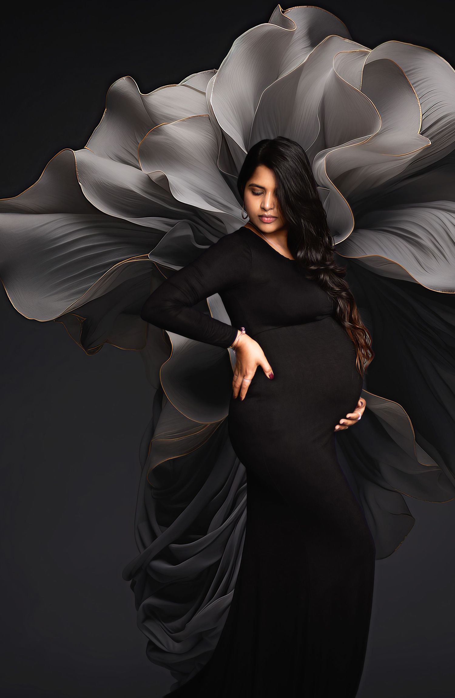 Dramatic maternity portrait with flowing black dress against grey floral backdrop.