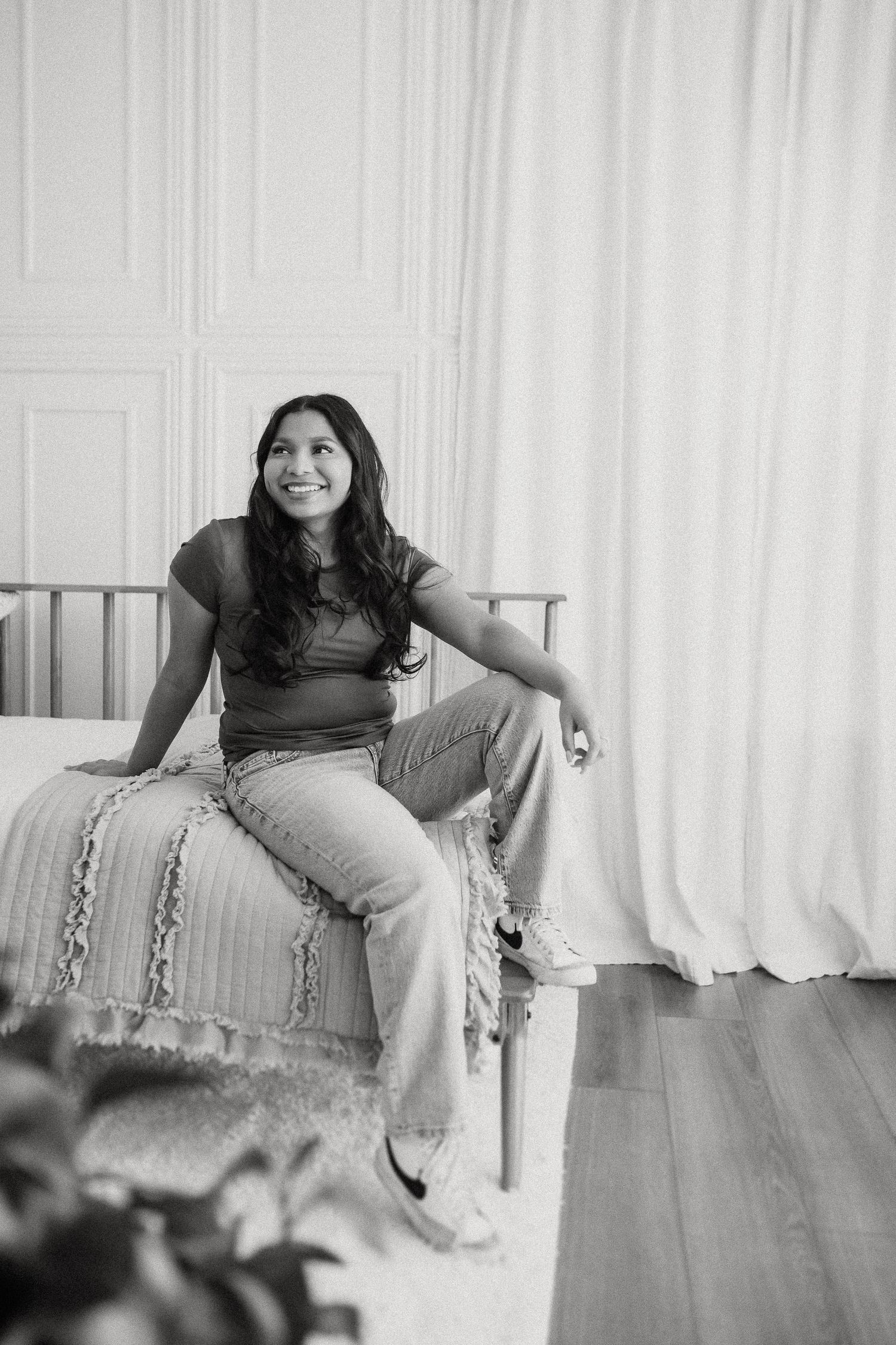 Black and white portrait of a casual model lounging on a daybed against white curtains in a bright room.