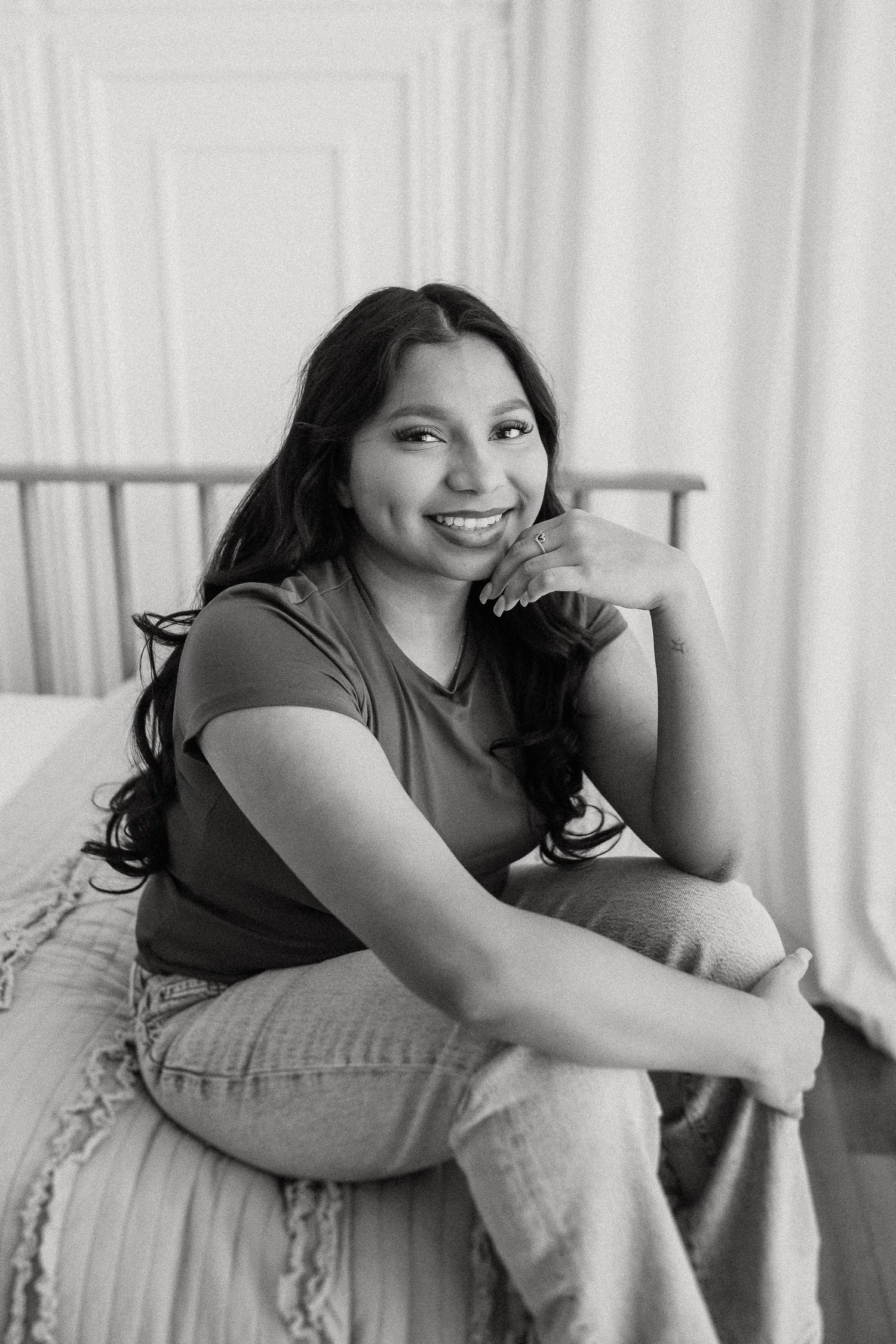 A casual portrait of someone sitting on a couch in casual attire with long dark hair in a black and white photo.