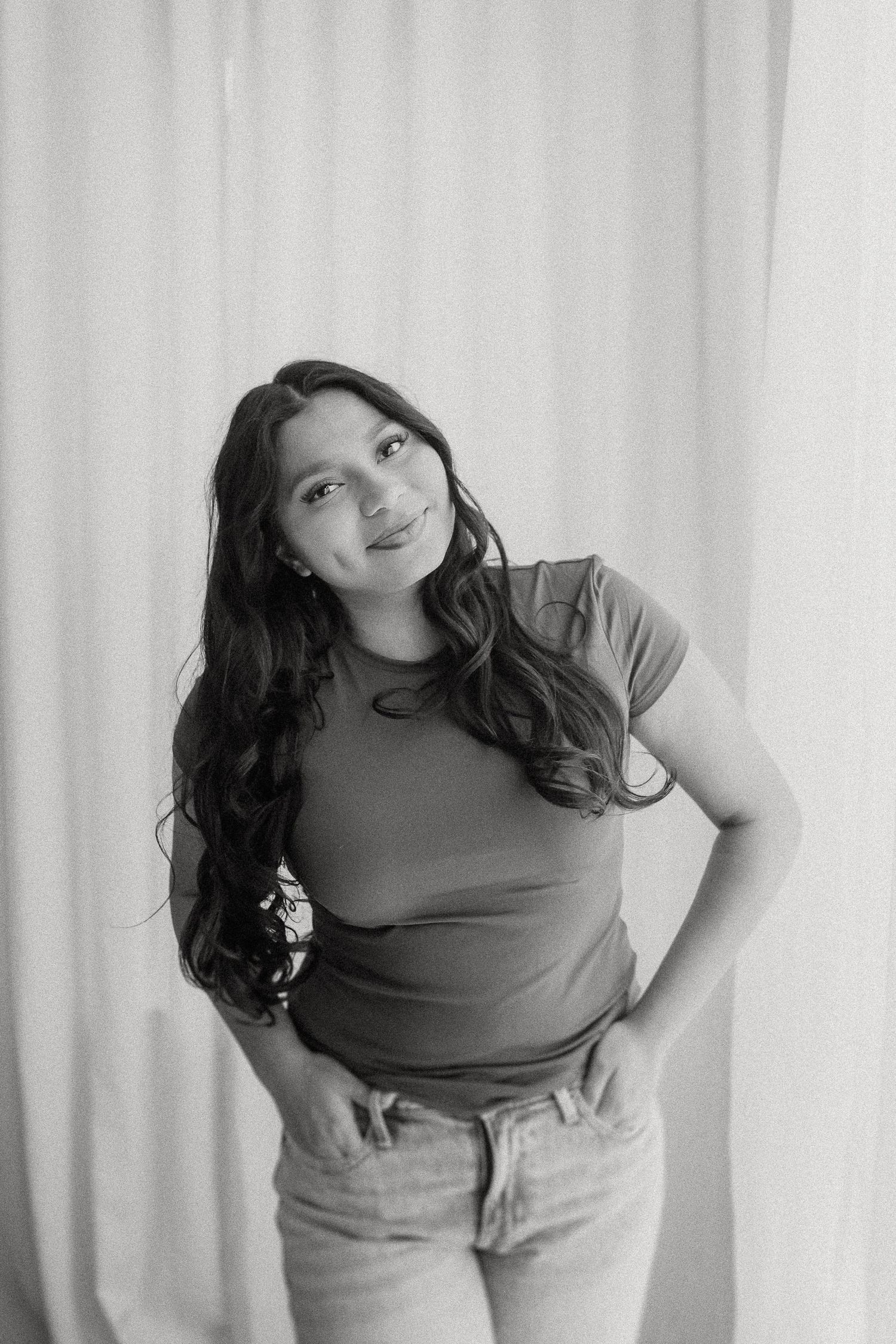 Black and white portrait of someone in casual attire posing against a light curtain backdrop.