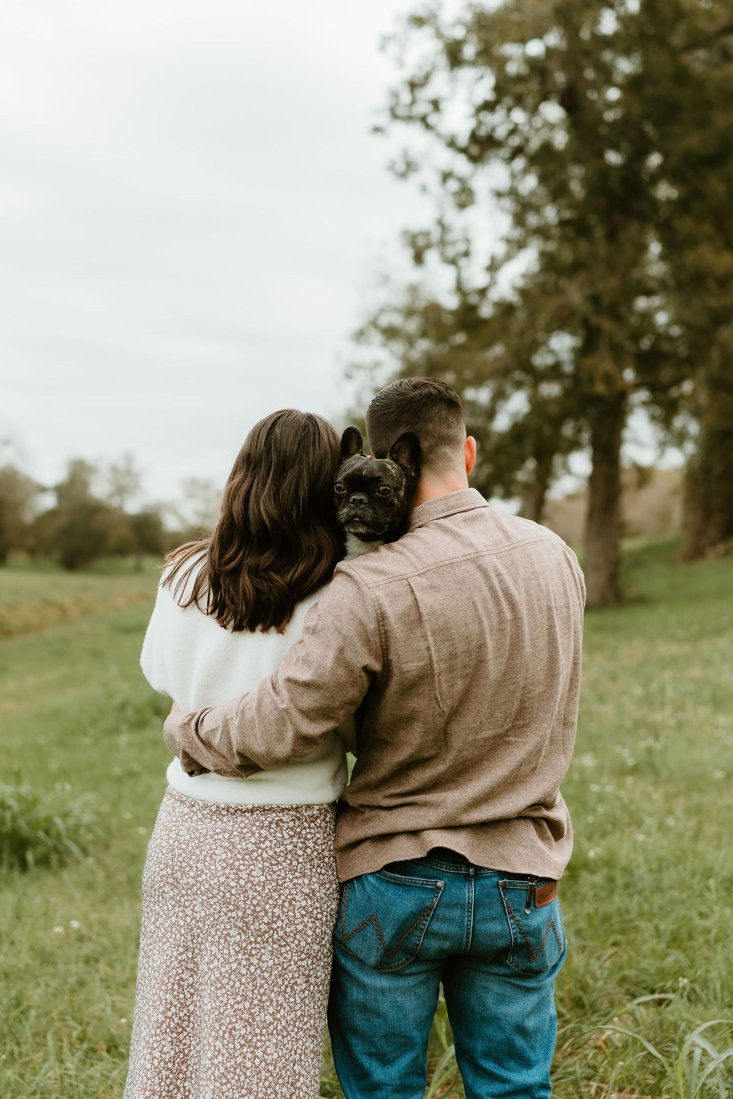 Couple embracing while standing in a grassy field during golden hour.