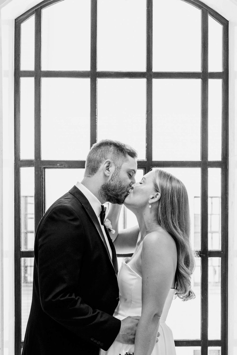 Black and white romantic photo of a couple about to kiss by a large arched window frame.