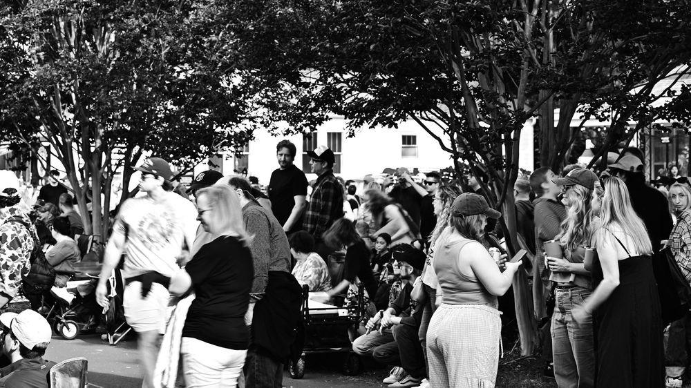 Black and white photo of a crowd gathered outdoors near trees at a community event or public gathering.