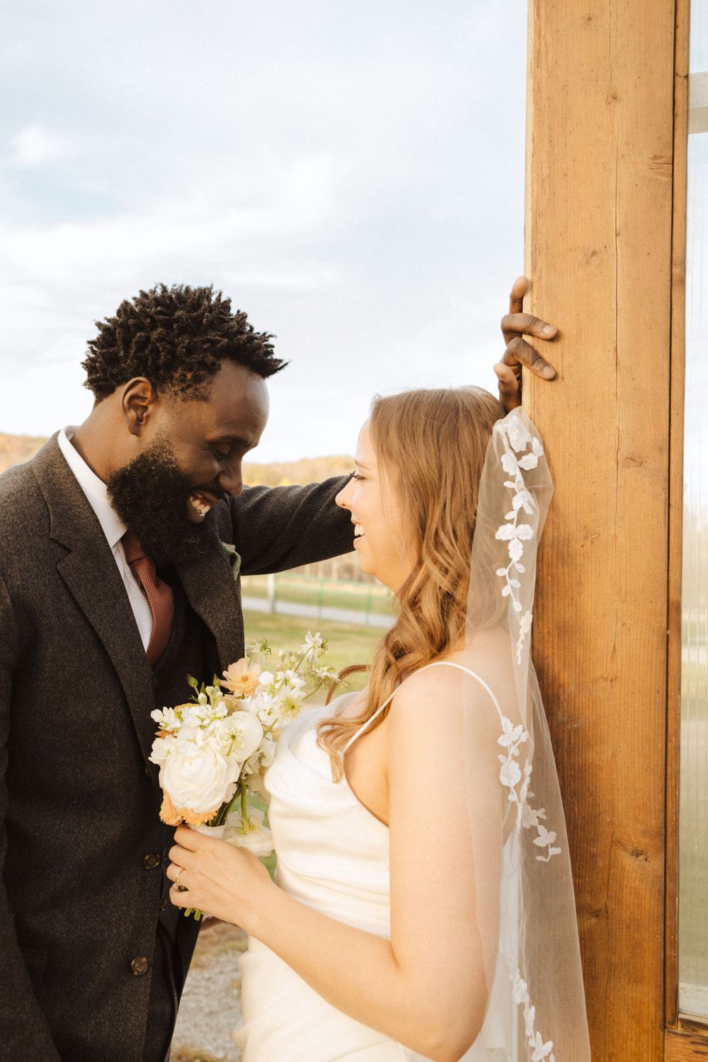 A couple in wedding attire share an intimate moment against a wooden post, with the bride holding a white bouquet near vernon nj.