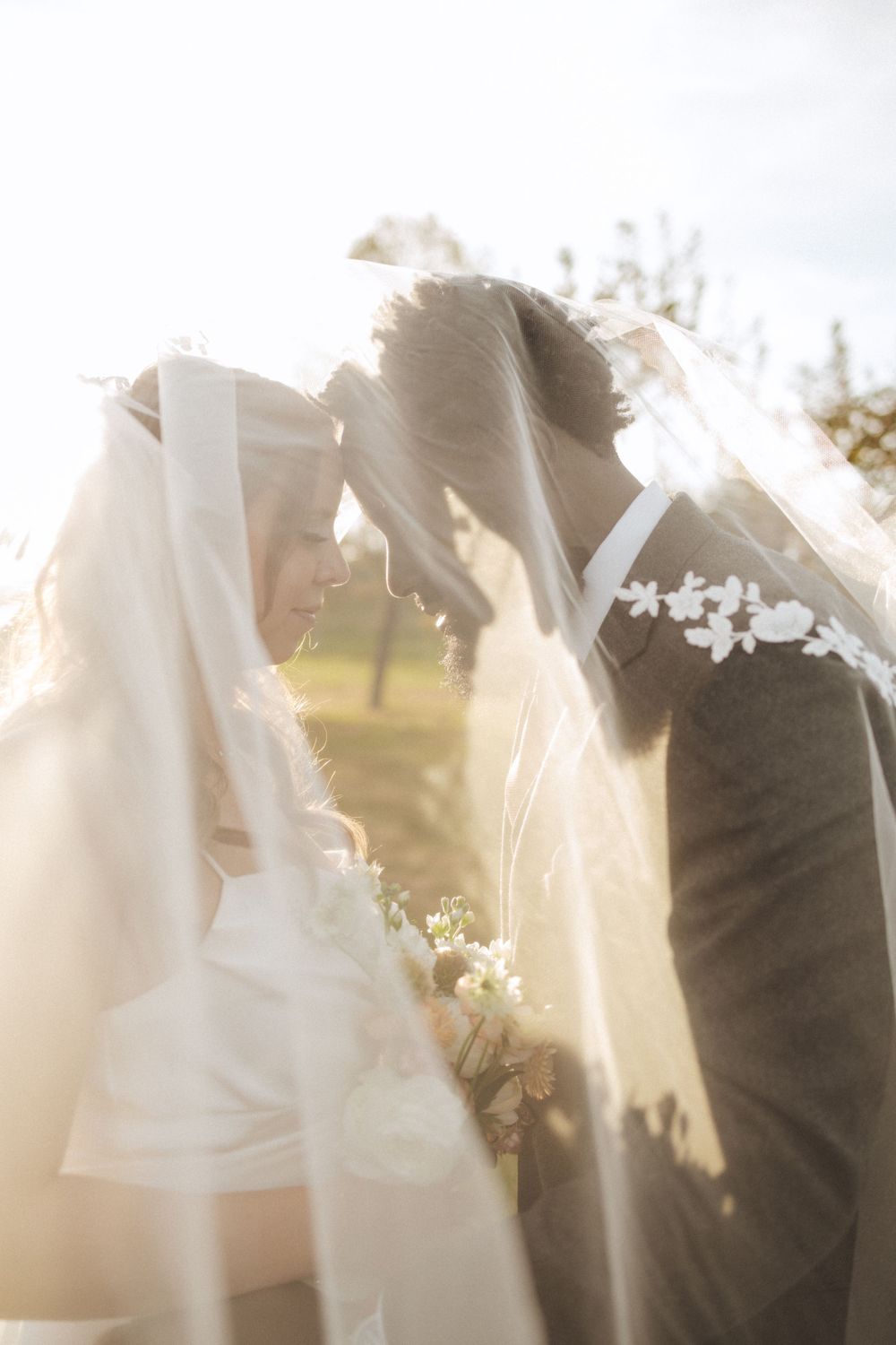 Romantic wedding couple shares intimate moment under flowing veil during outdoor ceremony in soft sunlight near vernon nj.