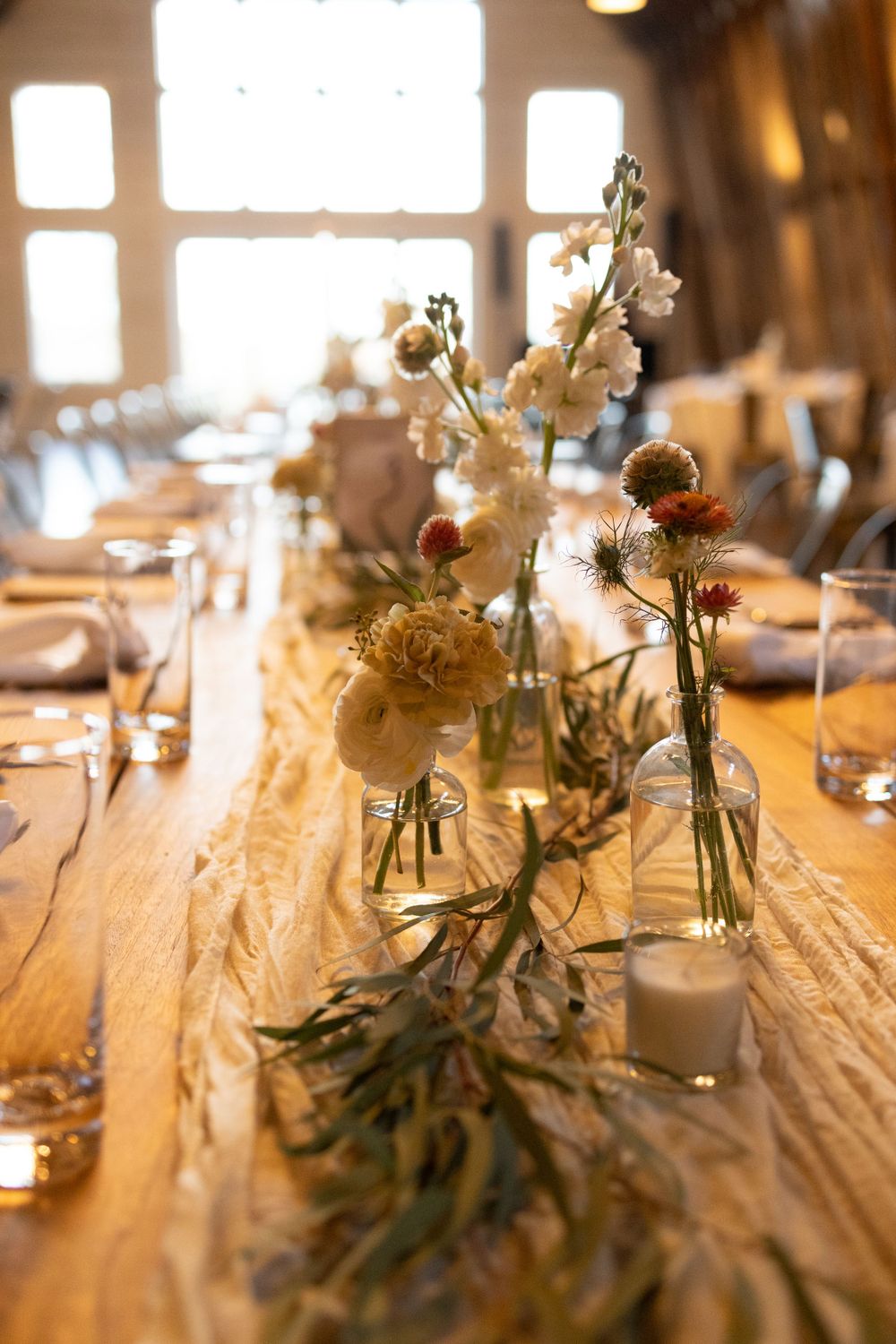 Rustic wedding reception table with delicate white flowers in glass vases and eucalyptus garland on wooden surface near vernon nj.