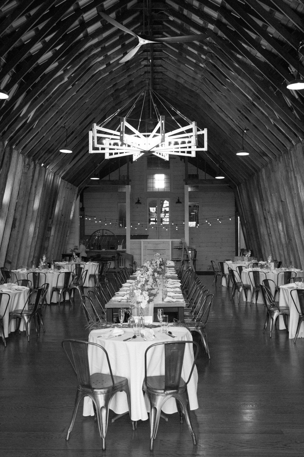 Black and white view of a rustic barn-style event venue interior set up with round tables and metal chairs for dining near vernon nj.