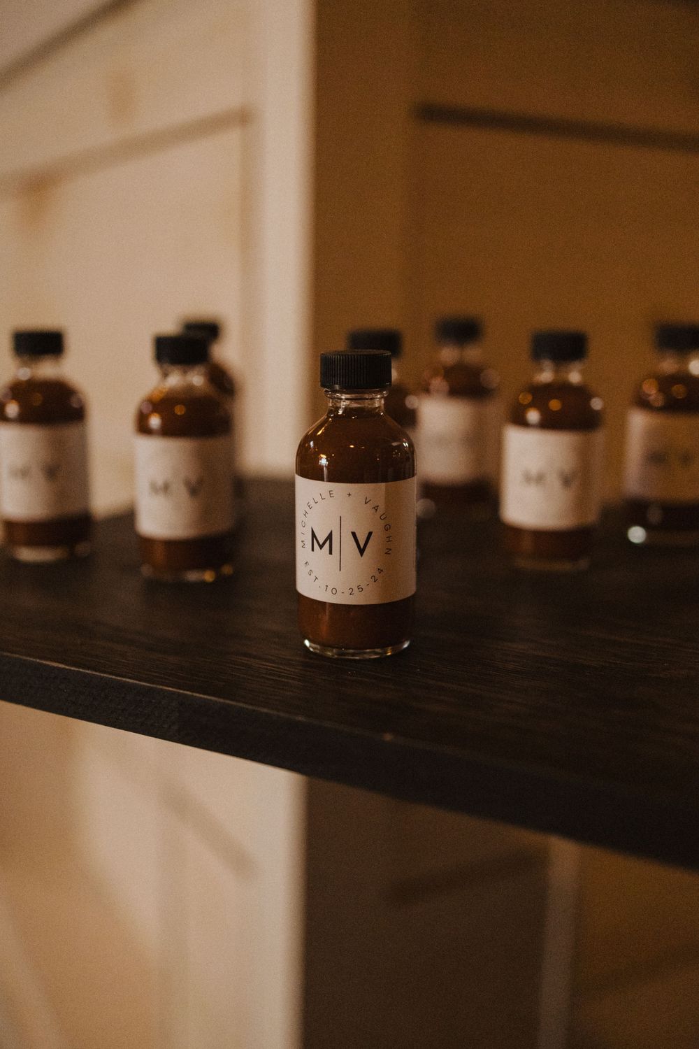 Small brown glass bottles with M V labels arranged on a dark wooden shelf in moody lighting near vernon nj.
