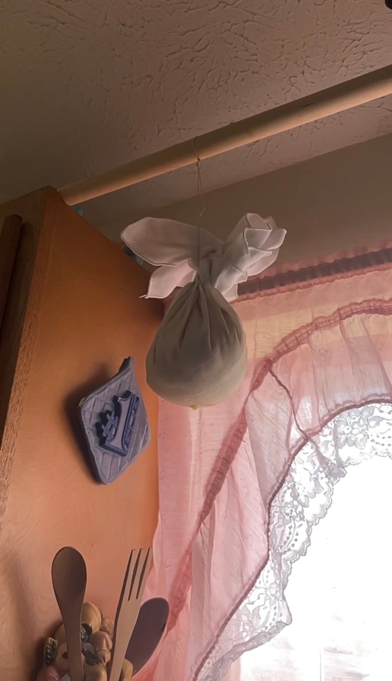 A sheer white fabric bundle hangs from a ceiling near an orange wall and decorative curtains.