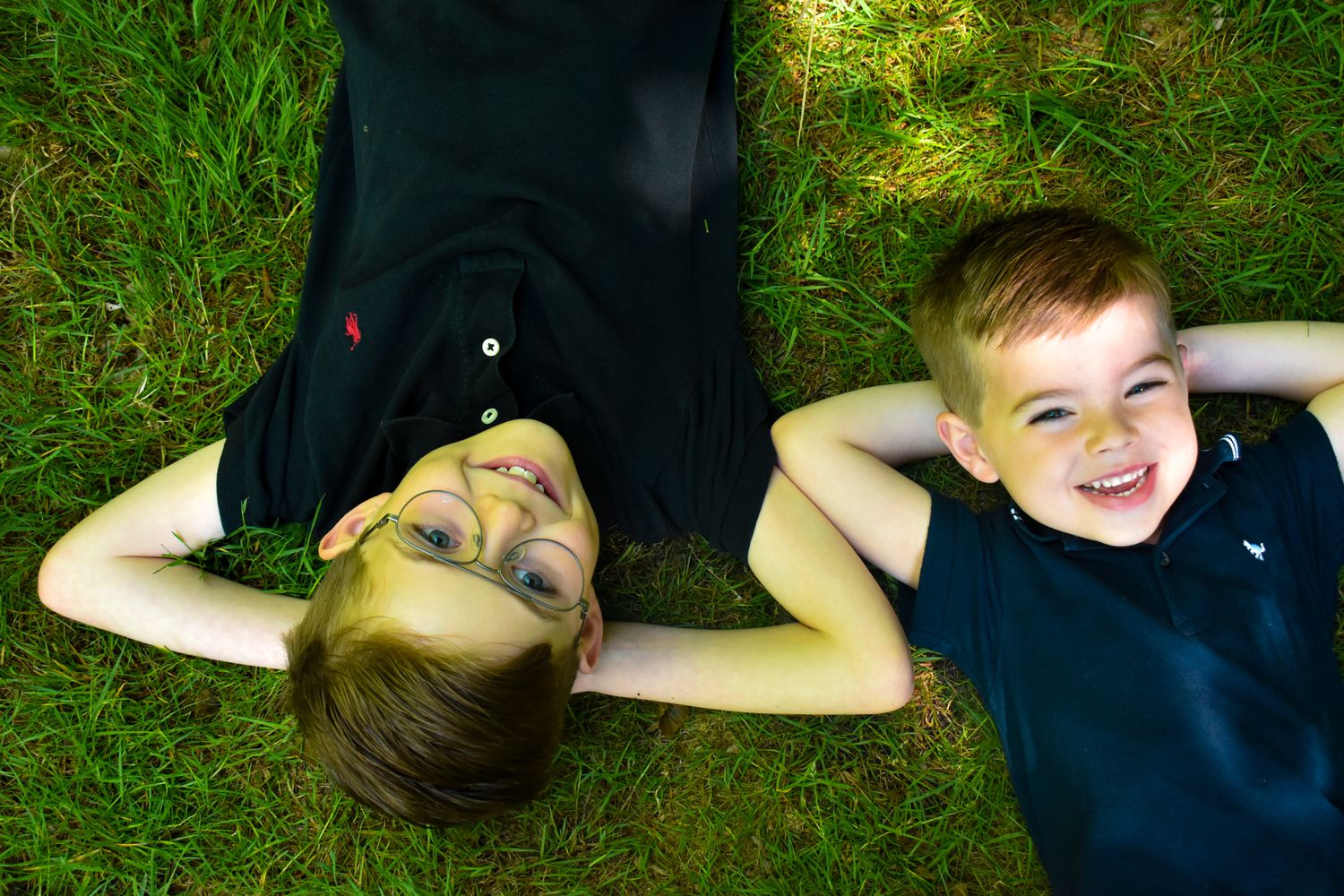 Two people lying on grass smiling at camera from above.