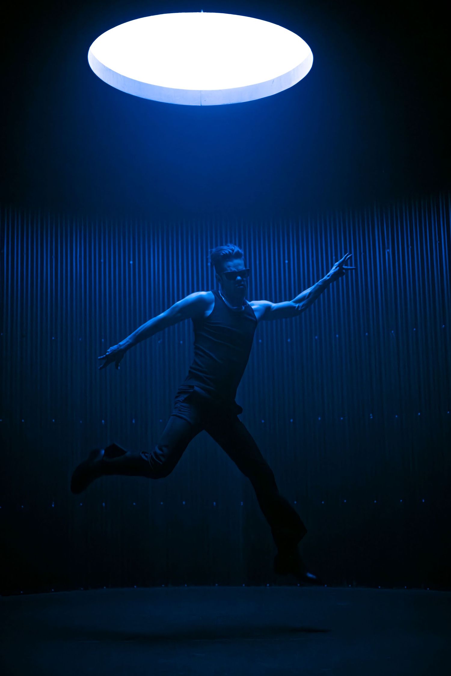 Figure in dramatic motion under circular lighting against dark background.