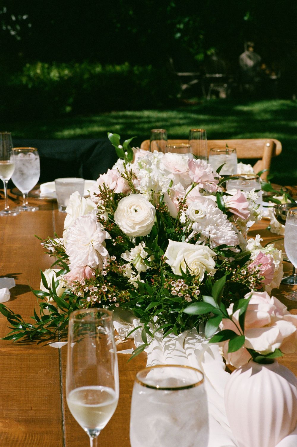 Elegant wedding table centerpiece with pink and white roses, greenery, and champagne glasses at an outdoor reception.