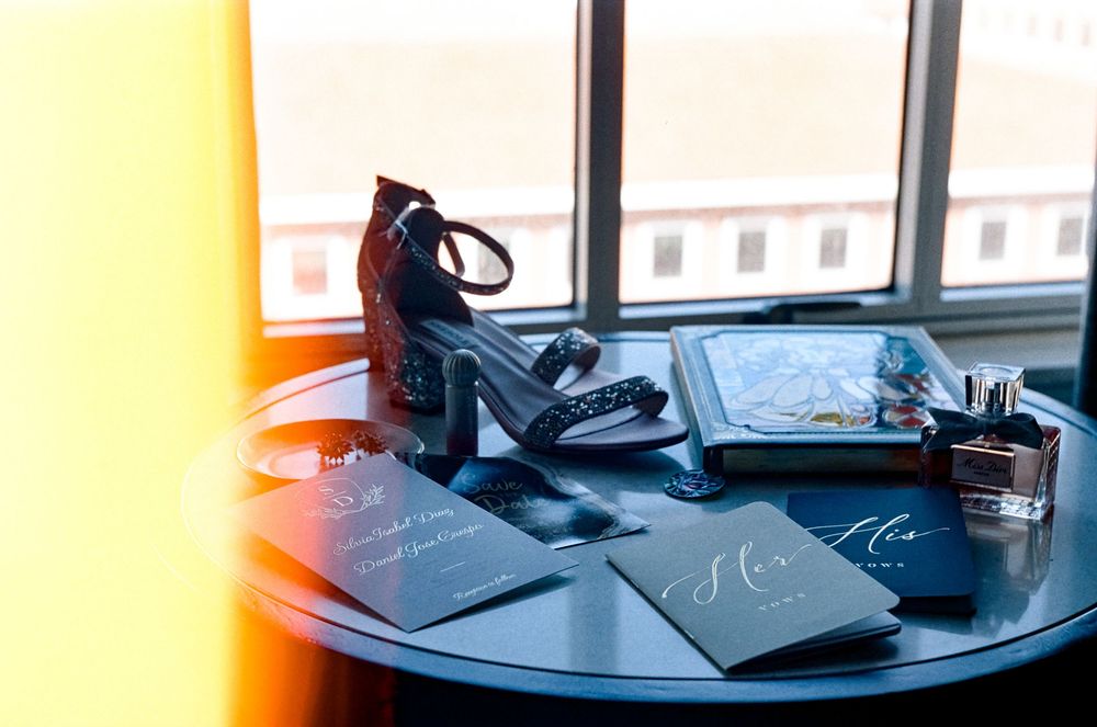 Black high heel shoes next to a tablet and papers on a round table with sunlight streaming through a window.