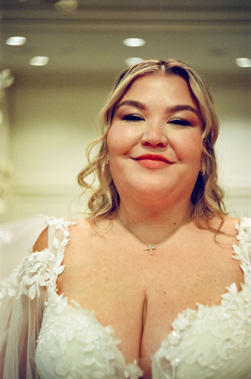 A close up portrait of someone wearing a white lace wedding dress with floral details.