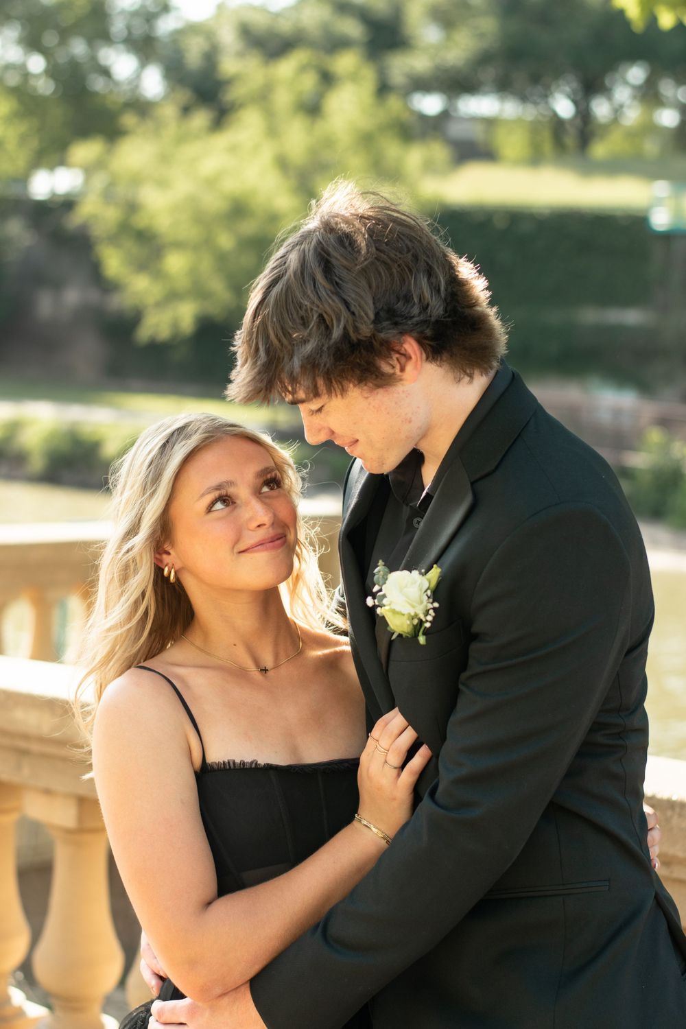 A couple in formal attire share an intimate moment by a stone balustrade in warm natural lighting.