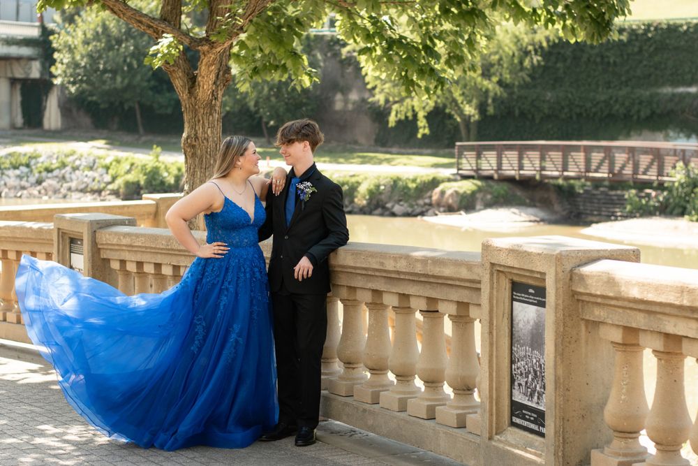 A couple poses against a stone balustrade with the bride wearing a flowing royal blue gown.