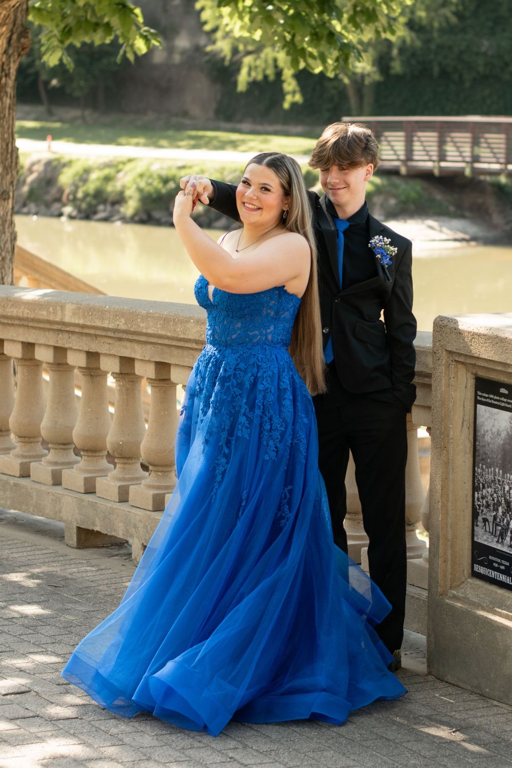 A formal couple poses on stone balcony, with person in bright blue ballgown and other in black suit for prom photos.
