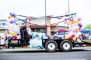 Long parade float trailer adorned with multicolored balloons and decorative elements.