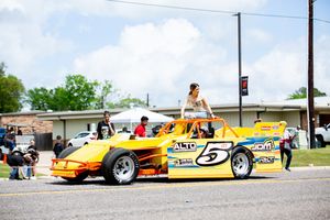 Row of bright yellow and orange dragsters and race cars parked on pavement.