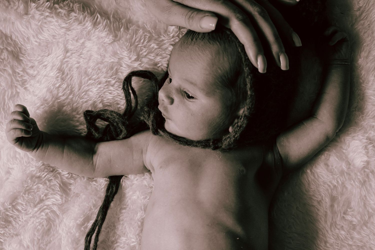 A mothers hand tenderly strokes the top of her newborn baby's head as the early morning light shines through the window.
