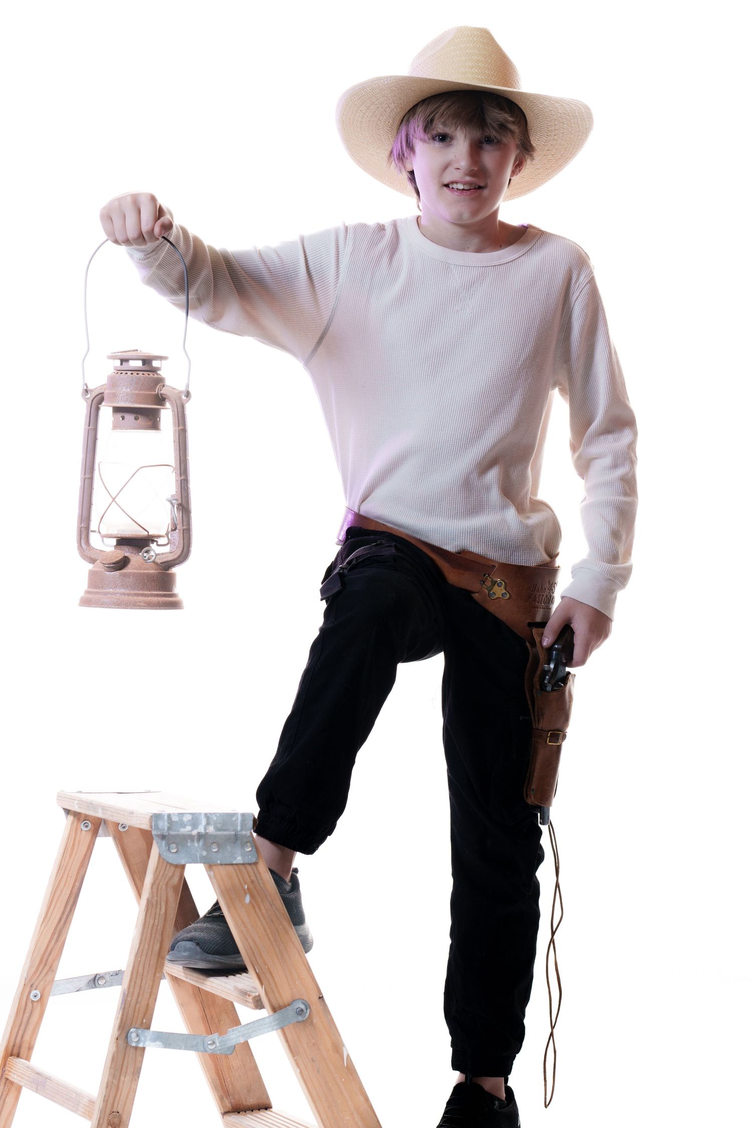 A person in a cowboy hat and white sweater poses on a stepladder while holding an antique lantern and toy gun.