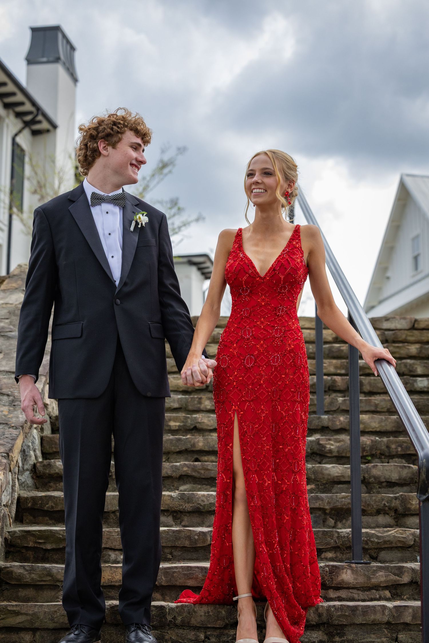 Couple in formal attire stands on stone steps outside elegant building.