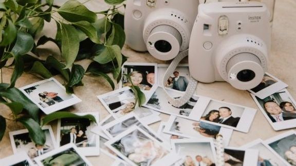 Wedding photography setup with instant cameras and scattered polaroid photos among green foliage.