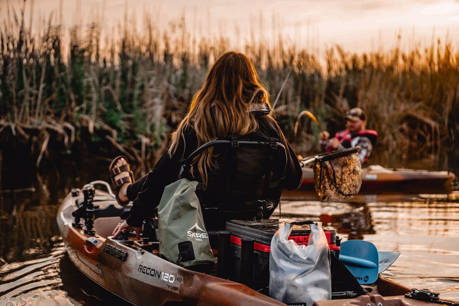 Kayakers explore peaceful lake waters during golden sunset among tall reeds.