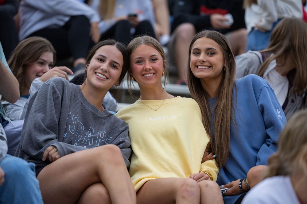 A crowd of spectators in casual clothing watch and smile during an outdoor event.
