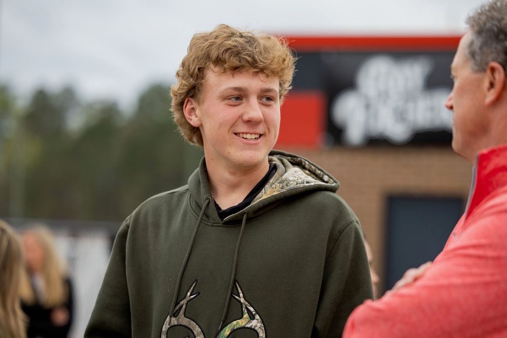 Young person in olive green hoodie with deer antler design smiling during outdoor conversation.
