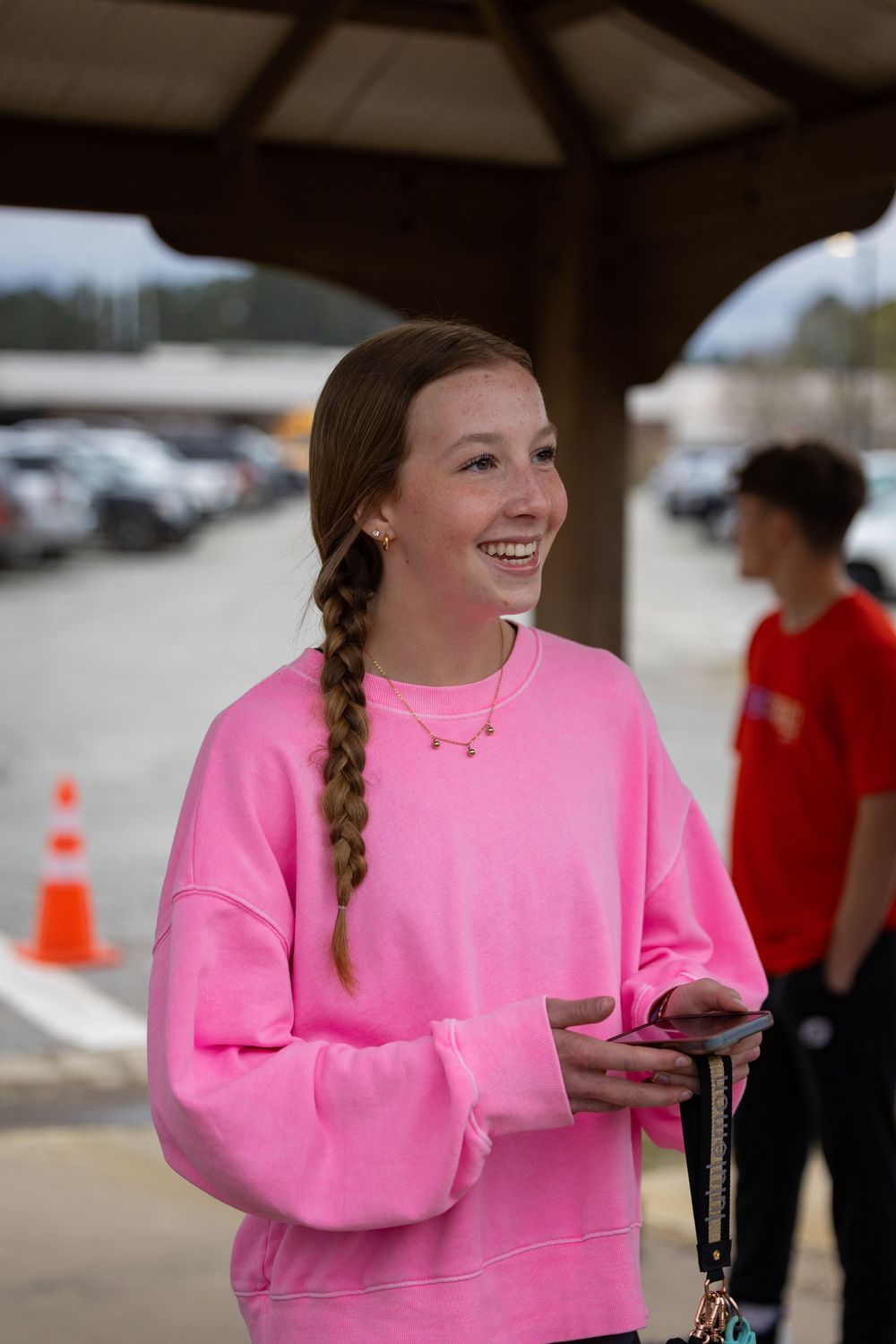 Person wearing bright pink sweatshirt is seen smiling and engaging with someone outside the frame.