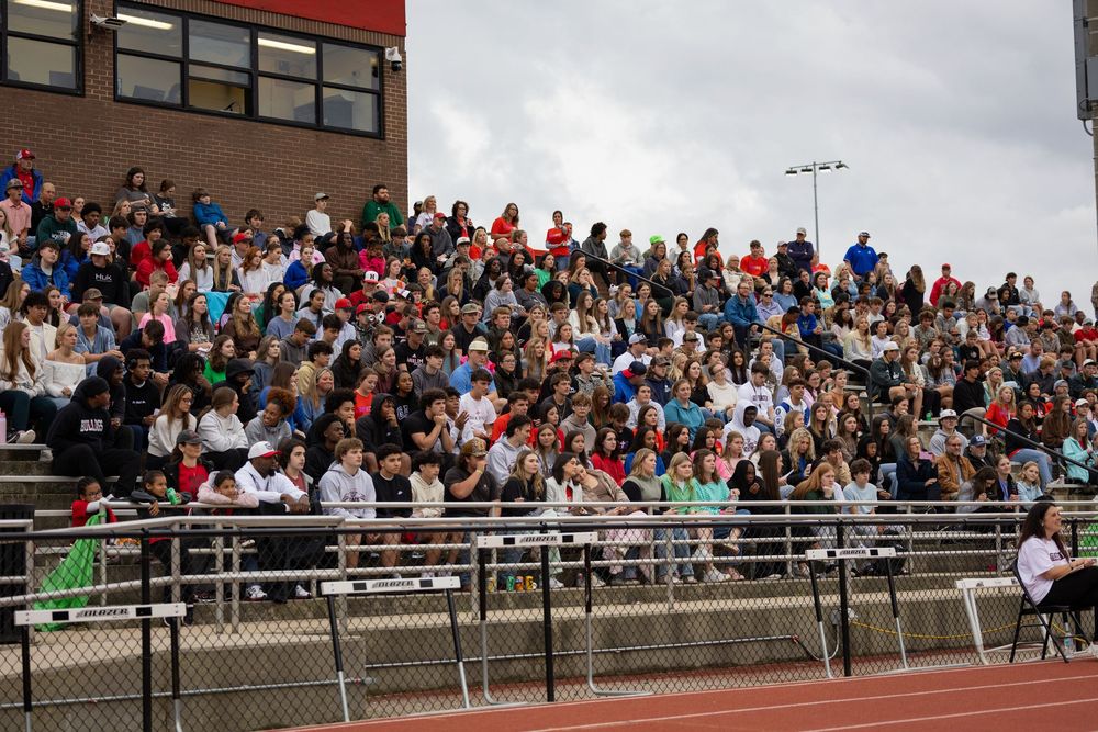 Large crowd of spectators fill bleachers at a sporting event during an overcast day.