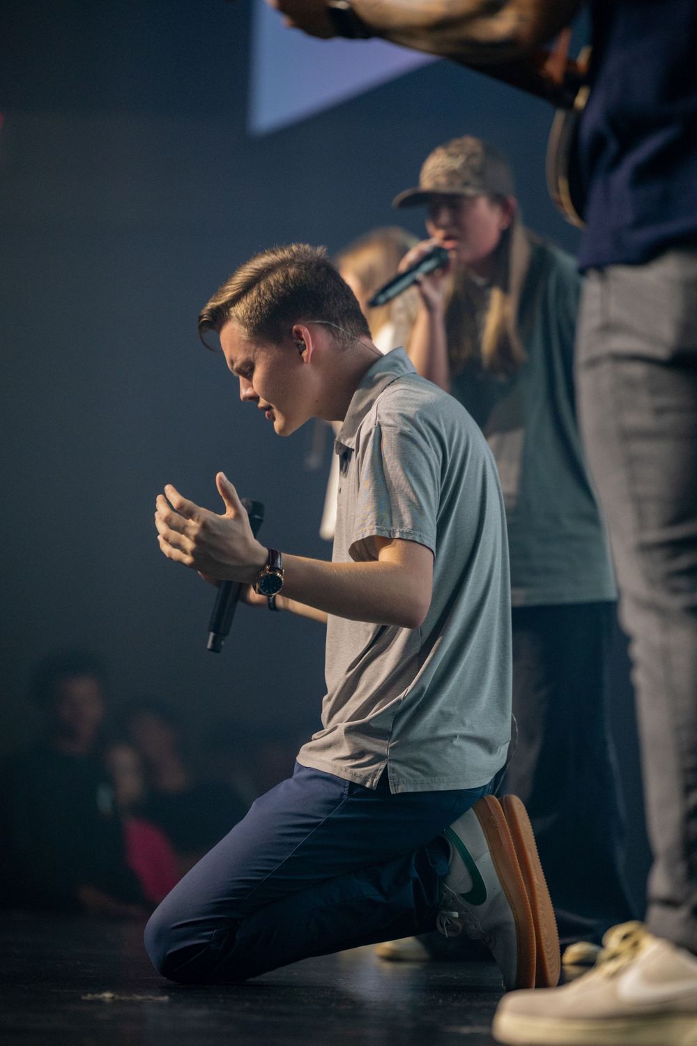 A vocalist kneeling on stage during a performance with dramatic lighting.