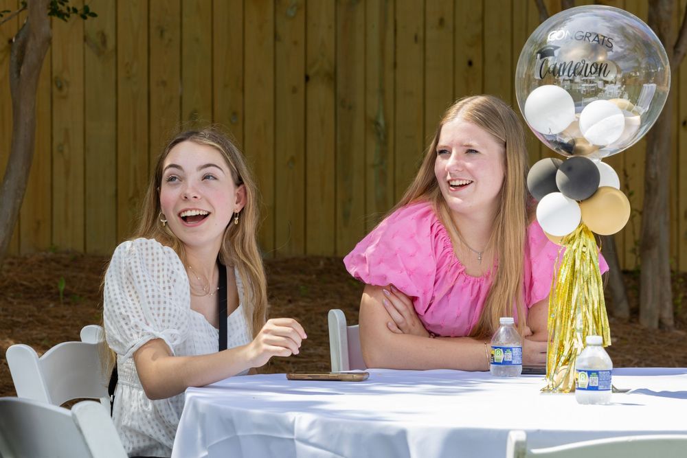 Two friends enjoy a celebratory moment with balloons and decorations at a party table outdoors.