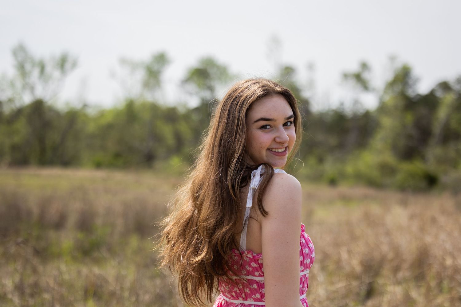 Person in beige shirt poses by lake with blooming tree branches in foreground.