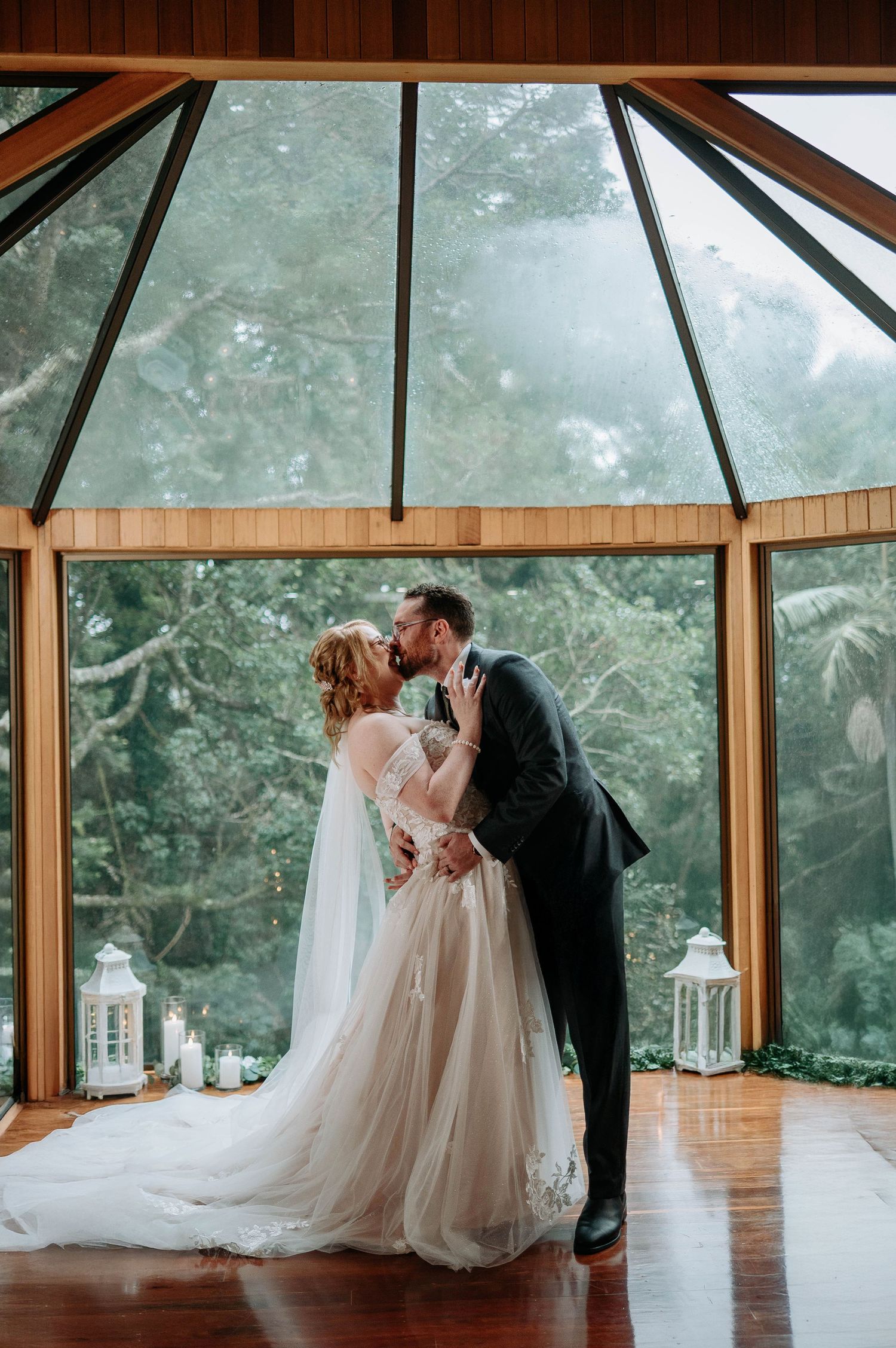 Romantic kiss in sunlit wooden pavilion with forest backdrop.