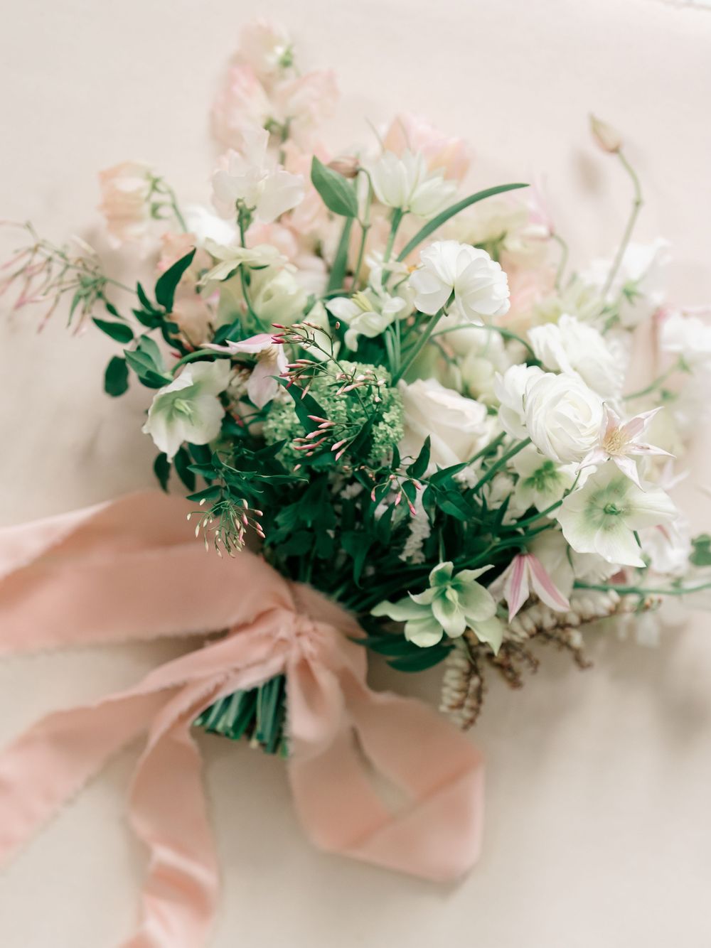 An elegant white floral bouquet with pink accents tied together with a blush pink silk ribbon on a light neutral background.