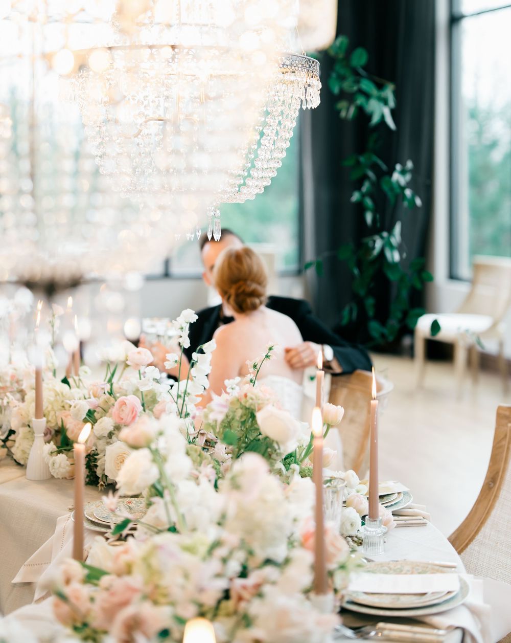 Elegant wedding reception table setting with crystal chandeliers, pink floral centerpieces and white place settings.