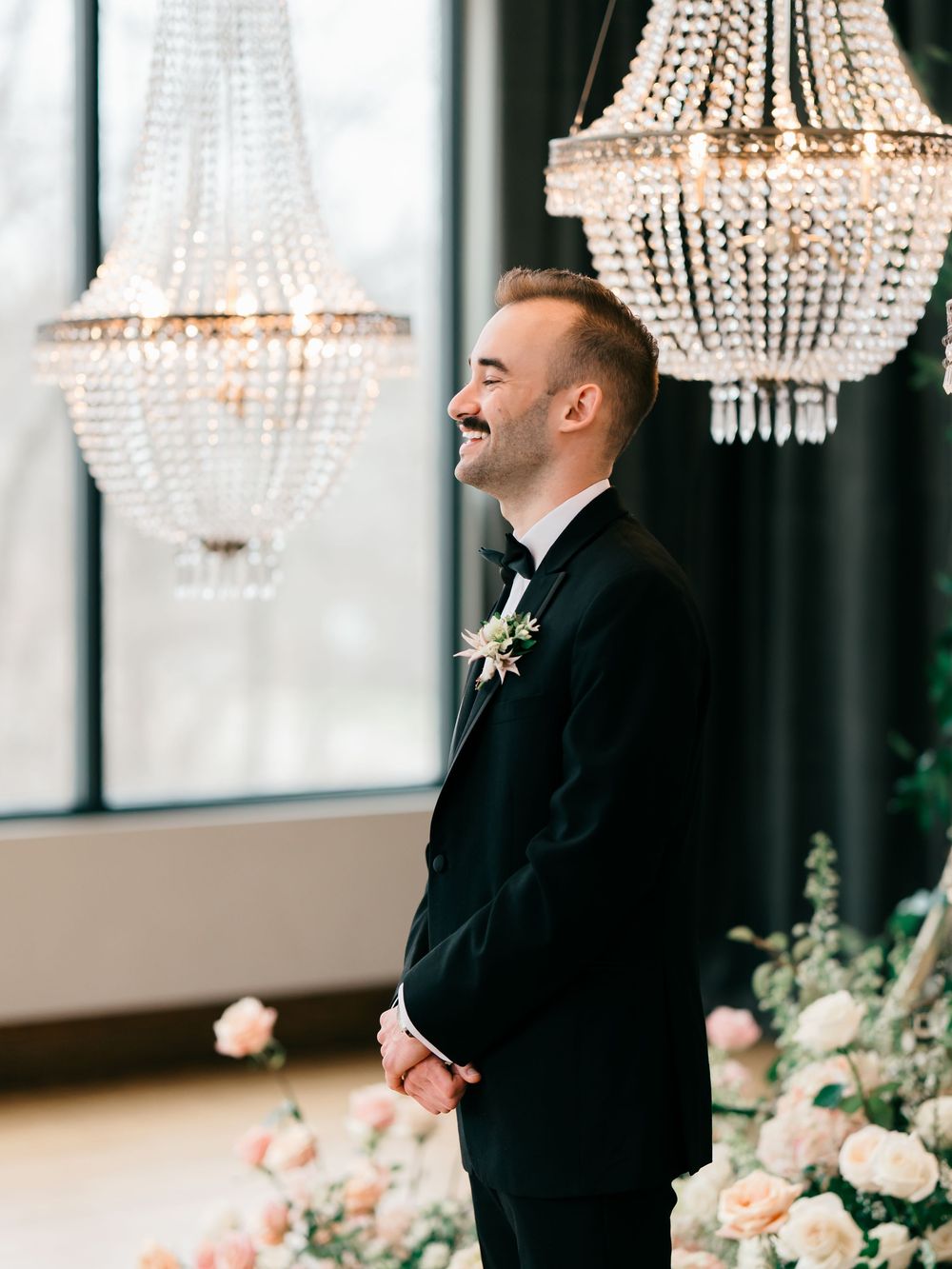Crystal chandeliers and pink floral arrangements create an elegant indoor setting for a formal wedding celebration.