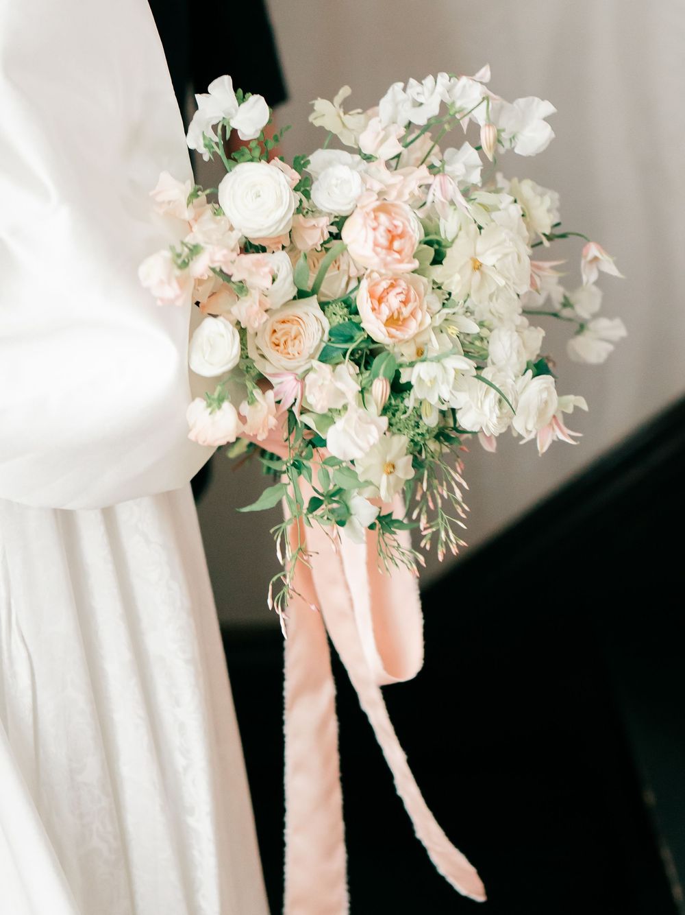 Elegant white and peach floral bouquet with roses and orchids tied with blush pink ribbons against a light background.