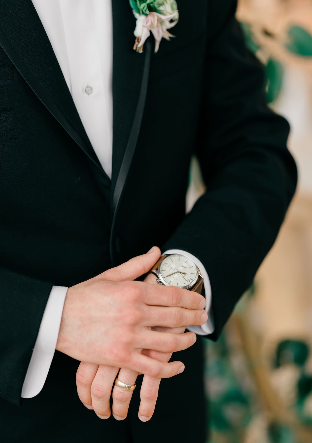 Close-up view of hands wearing wedding rings and formal black tuxedo sleeve.