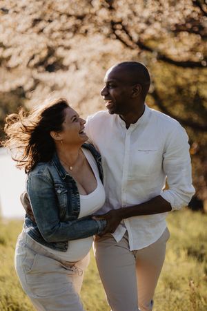 Playful outdoor maternity photos with couple laughing in casual attire.