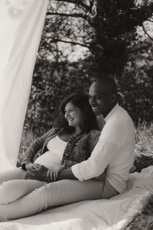 Intimate black and white maternity photos with couple relaxing on white bedding.