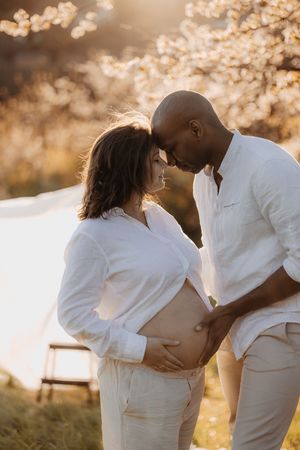 Romantic maternity photoshoot in golden sunset light with couple in white outfits.