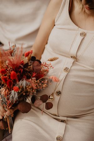 A dried floral arrangement with red blooms next to cream-colored fabric with buttons.